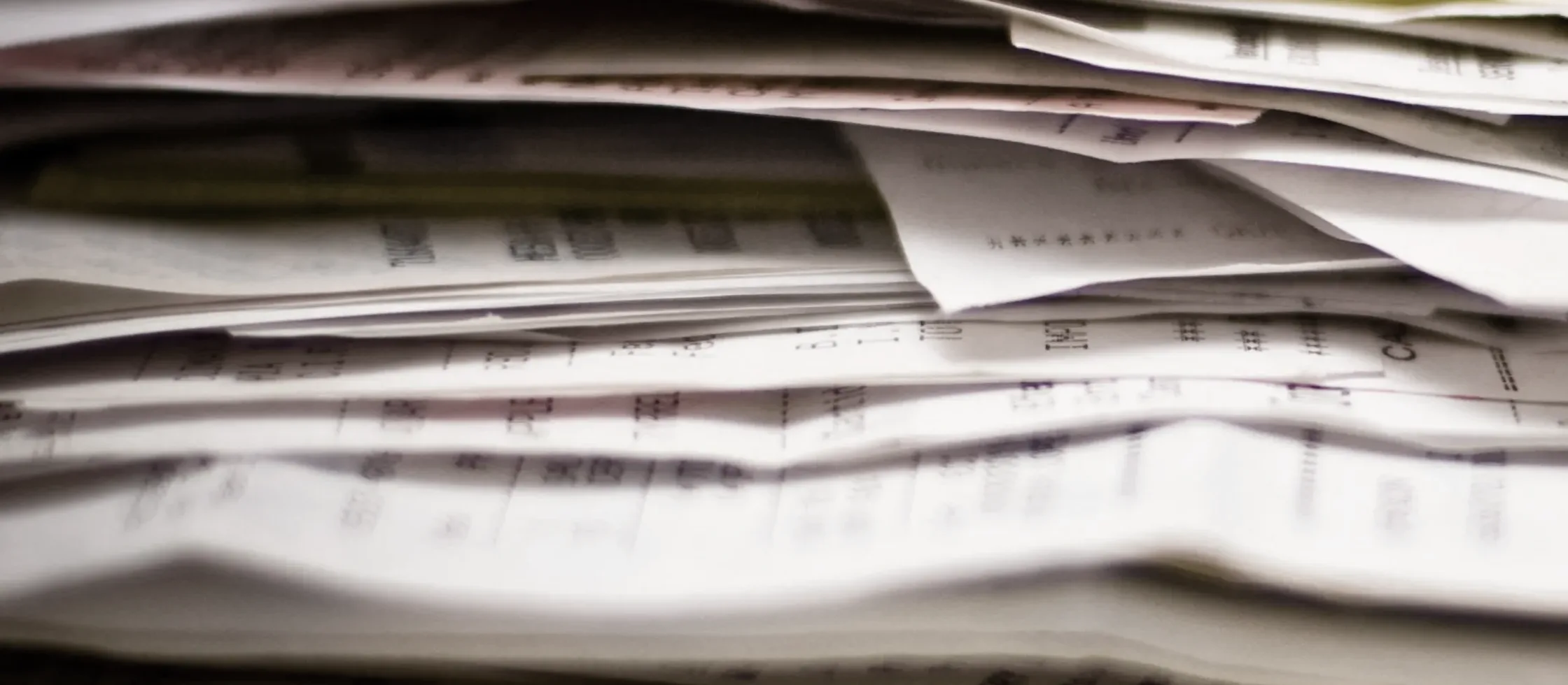 A thick stack of paper dockets and invoices seen edge on, the printing too shallow in focus to read.